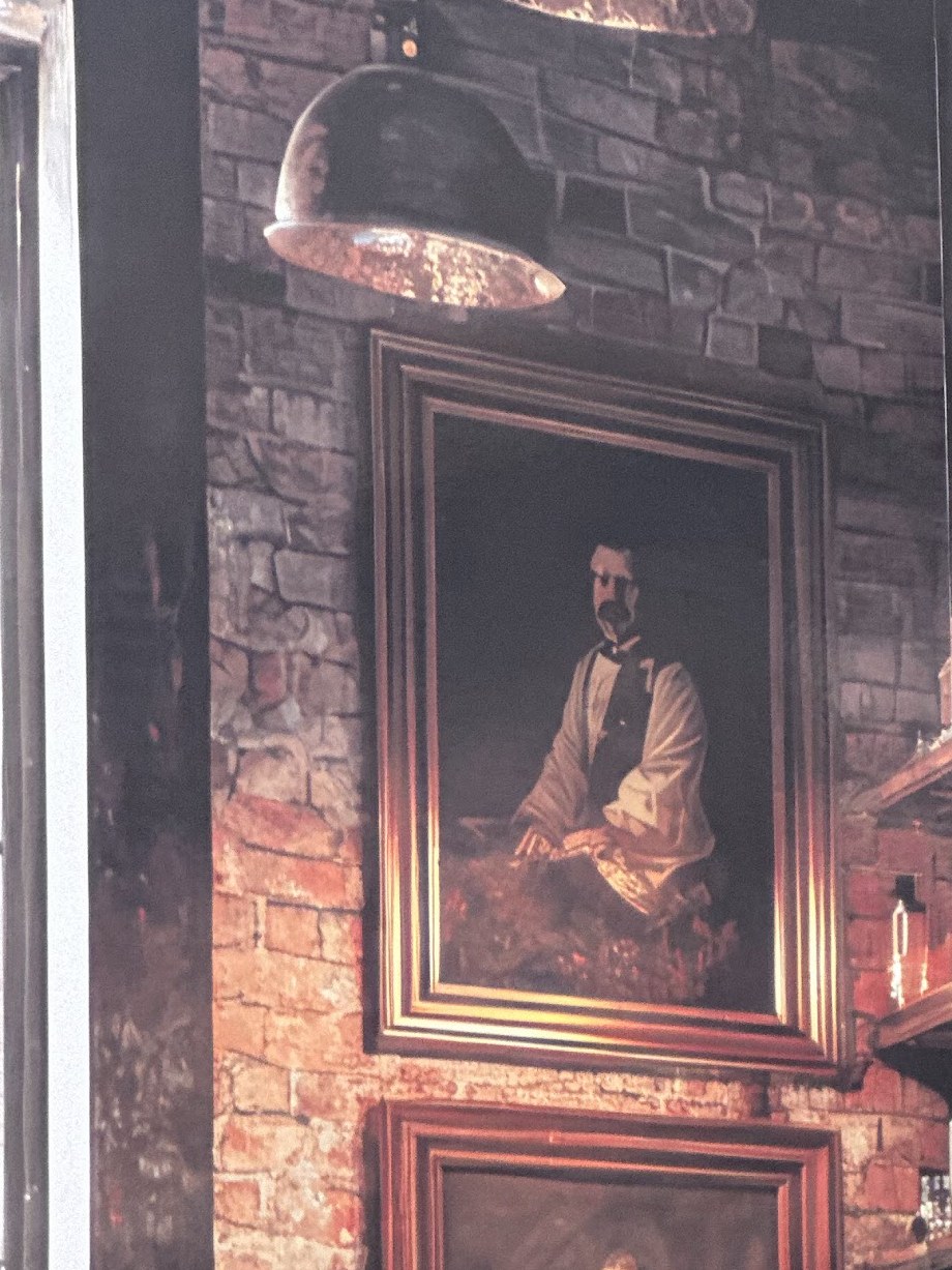 De zithoek voorin: een portret in een gouden lijst aan de bakstenen wand, met een koperen hanglamp