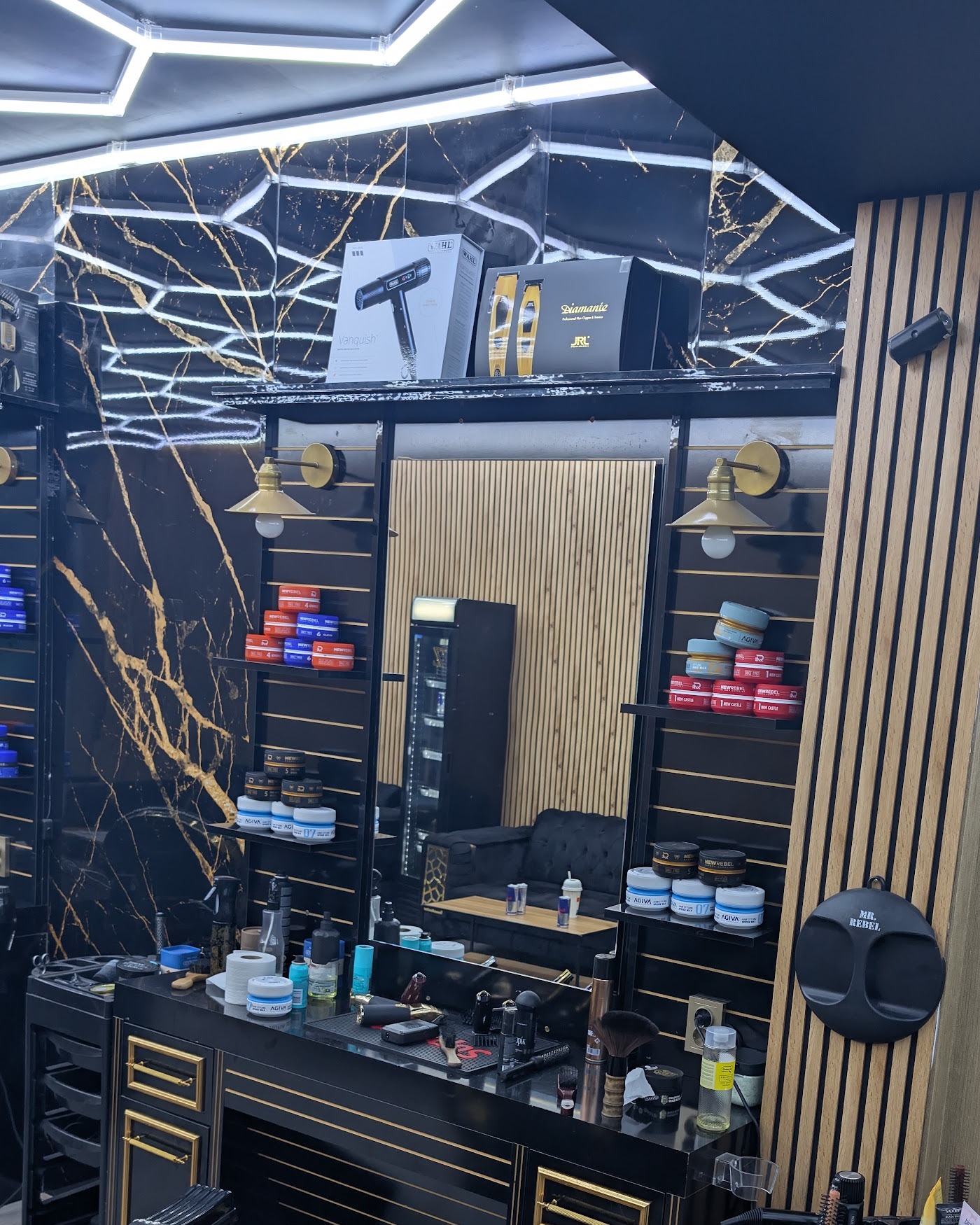 Werkstation met spiegel, messing wandlampen, schappen vol pomades, de marmeren wand en het hexagon-plafond