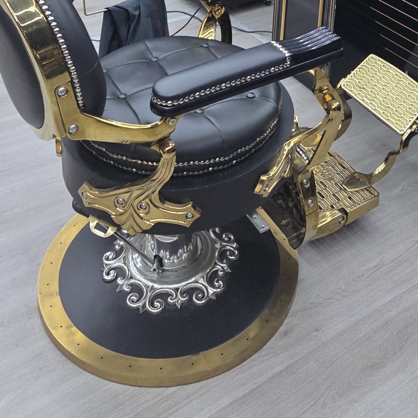 Close-up van de zwart-gouden barbierstoel met zijn gouden voetstuk en versierde voet
