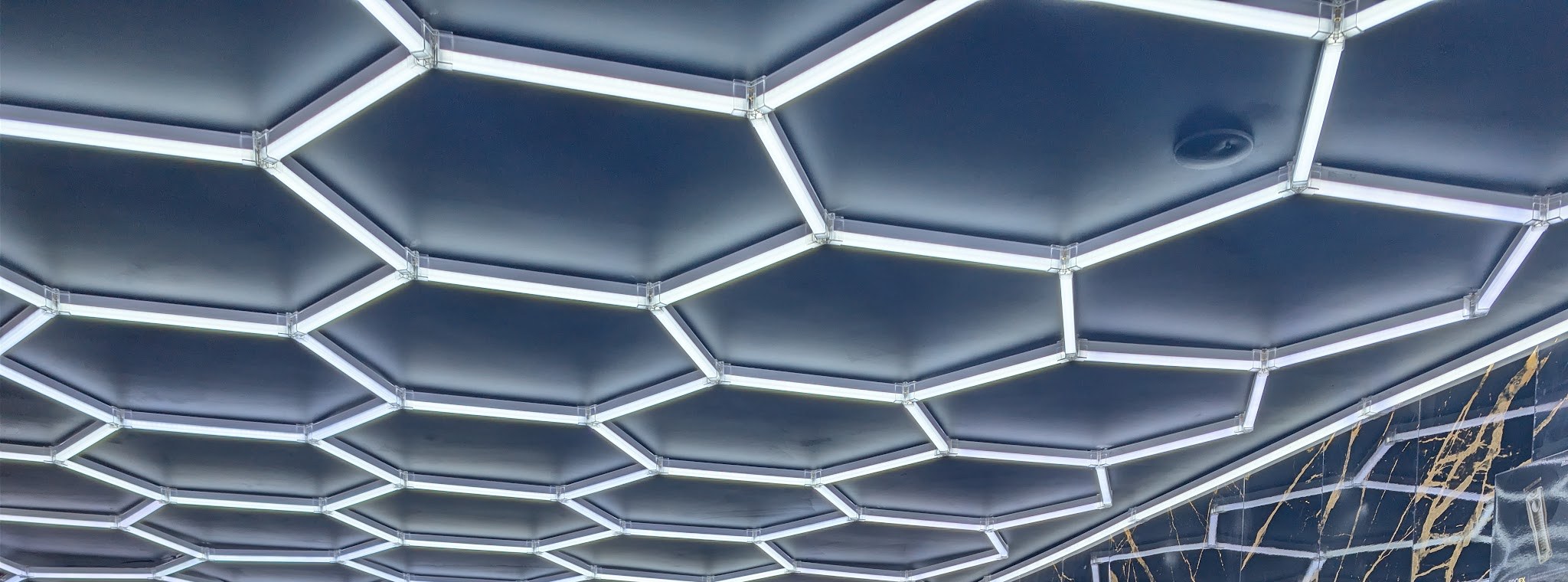 Het hexagon-LED-plafond van de zaak, met rechts de wand van zwart marmer met gouden aders