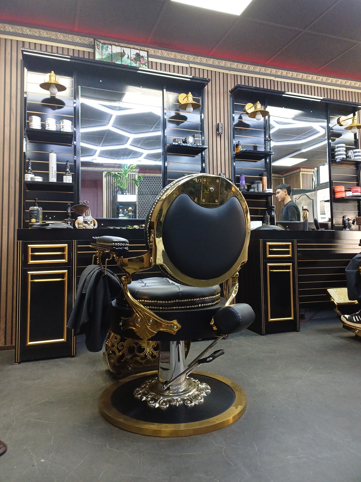 De zwart-gouden barbierstoel van Zerewan Kapsalon voor de spiegelwand met pomades, onder het hexagon-plafond